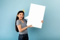 Cheery Indian teen girl holding empty speech bubble, offering space for advertisement on blue studio background, mockup Royalty Free Stock Photo