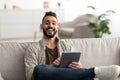 Cheery young Arab guy using digital tablet, learning or working remotely, having online meeting at home Royalty Free Stock Photo