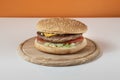 Cheesburgher on wooden plate isolated and centred on white table and orange wall