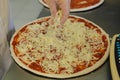 Cheese being spread on tomato sauce on pizza base