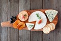 Cheese board with a selection of cheeses, crackers, figs and grapes, above view on wooden serving board