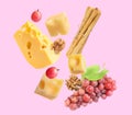 Cheese, breadsticks, grapes and walnut falling against light pink background