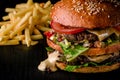 Cheese burger with grilled meat, cheese, tomato and potatoes on dark wooden surface. Ideal for advertisement. Close-up Royalty Free Stock Photo