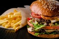 Cheese burger with grilled meat, cheese, tomato and potatoes on dark wooden surface. Ideal for advertisement. Close-up Royalty Free Stock Photo