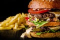 Cheese burger with grilled meat, cheese, tomato and potatoes on dark wooden surface. Ideal for advertisement. Close-up