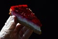 Cheese cake with red strawberry jelly on top held in left hand in hygienic latex glove, dark background Royalty Free Stock Photo