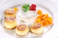 Cheese cakes with sour cream, slices of sweet peach, mint and red currants on a white plate