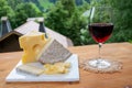 Cheese collection, Swiss cow cheese emmental, tomme, glass of red wine from Savoie and mountains village in Apls on background Royalty Free Stock Photo
