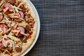 Close up of freshly home made pizza on a white plate with cheese, meat, onions, spicy products. Italian traditional food