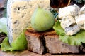 Cheese with mold on a green lettuce leaf with figs on a wooden background. Golden shot glass with alcohol