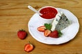 Cheese with a noble blue mold on plate with strawberries and with strawberry sauce, mint, on a wooden background. Top view with co