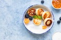 Cheese pancakes, fritters or syrniki with blueberry, physalis and yogurt, blue background. Healthy and tasty breakfast