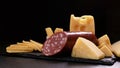 cheese and piece of salami loaf are on black stone board on dark background