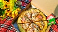 A cheese pizzas on a red checkered cloth decorated with artificial sunflowers