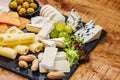 Cheese plate. Assorted different types of cheese with olives, grapes and chips on a black plate on a wooden table,assorted cheeses Royalty Free Stock Photo