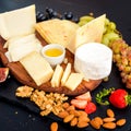 Cheese plate. Assortment of cheese with walnuts, almonds, grapes, figs, strawberries, blueberries and honey on a stone Royalty Free Stock Photo