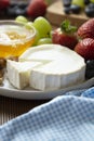 Cheese plate round sliced soft cheese, blueberry, strawberry, grapes and honey on wooden table Royalty Free Stock Photo