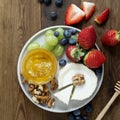 Cheese plate round sliced soft cheese, blueberry, strawberry, grapes and honey on wooden table, flat lay. Square image Royalty Free Stock Photo