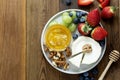 Cheese plate round sliced soft cheese, blueberry, strawberry, grapes and honey on wooden table, flat lay Royalty Free Stock Photo