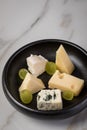 Cheese plate with selection Edamer, Parmesan, goat, blue and cream cheese, peer and grapes on black dish and marble background