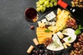 Cheese platter with craft cheese assortment, grape and red wine at black background. Royalty Free Stock Photo