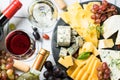 Cheese platter with craft cheese assortment and wine glasses at white tile background.