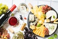 Cheese platter with craft cheese assortment and wine glasses at white tile background.