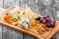 Cheese platter garnished with pear, honey, walnuts, grapes, carambola, physalis on cutting board on wooden background Royalty Free Stock Photo