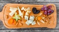 Cheese platter garnished with pear, honey, walnuts, grapes, carambola, physalis on cutting board on wooden background