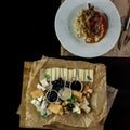 Cheese platter stands on a wooden table in a restaurant next to a duck leg in a sauce. Easy tasty snack. Useful lunch in a cafe.