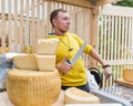 A cheese seller in a yellow sweater offers cheese to a customer