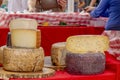 Stacked rounds of cheese are displayed at the outdoor farmers market while people shop