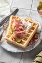 Cheese waffles with ham, cream cheese and cucumber with cutlery and linen napkin on gray tile background. Delisious