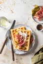 Cheese waffles with ham, cream cheese and cucumber with rustic cutlery and linen napkin on beige textured background