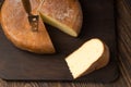 Cheese wheel and slice on a cutting board over a wooden table on Royalty Free Stock Photo