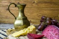 The cheese is yellow and red, a bunch of grapes, a bronze jug stands on a wooden background