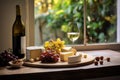 Cheeseboard with assorted cheese, grape near wineglass with white wine on table near window