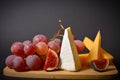 Cheeseboard platter with hard and soft mould cheese, grape and segmented fig on wooden board