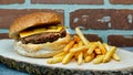 Cheeseburger with cheddar chese, russian salad, pickled cucumbers, french fries on wooden tray with brick wall background Royalty Free Stock Photo