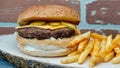 Cheeseburger  with cheddar chese, russian salad, pickled cucumbers, french fries on wooden tray with brick wall background Royalty Free Stock Photo