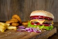 Cheeseburger, french fries and onion rings on wooden chopping board over wooden backdrop Royalty Free Stock Photo