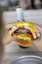 Cheeseburger with ham, fried egg, lettuce, tomato and onion, bitten by a person holding it in his hands