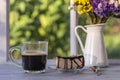 Cheesecake with chocolate sauce and glass cup of black coffee on a wooden table near window. Coffee time with slice of cake at