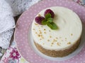 Cheesecake with raspberries and mint on a pink plate on a wooden table with floral fabric and laces. Close up, copy space Royalty Free Stock Photo