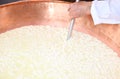 Cheesemaker stirs the curds into the copper cauldron to make che