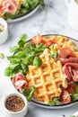 Cheesy belgian waffles served with ham, tomatoes and lettuce corn close up on white marble background . Savory waffles
