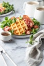 Cheesy belgian waffles served with ham, tomatoes and lettuce corn with cutlery on white marble background . Savory