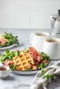 Cheesy belgian waffles served with ham, tomatoes and lettuce corn on white marble background with text space. Savory