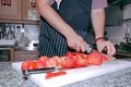 Chef in apron cutting peeled tomato on a board in the kitchen