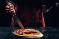 Chef in apron with meat fork and knife slicing gourmet grilled steaks with rosemary and chili pepper on wooden board Royalty Free Stock Photo